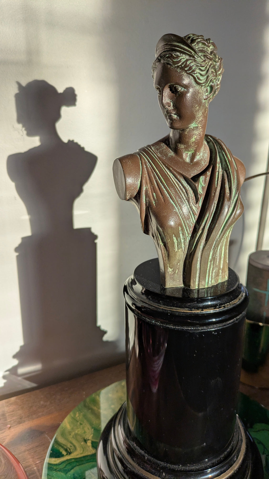 Bronze bust of a classical figure on a dark pedestal with a blurred background