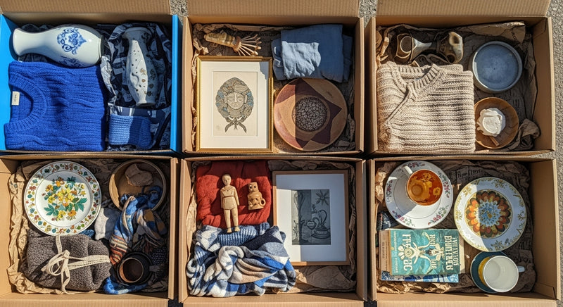 Collection of decorative items including plates, figurines, and textiles arranged in a box.